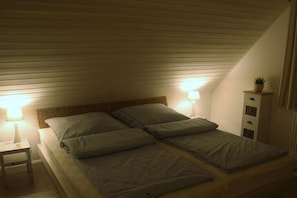 A single bed in a room with sloped ceilings, two bedside lamps, a small table, and a cabinet with drawers. - Frisian happiness in Greetsiel (Greetsiel)
