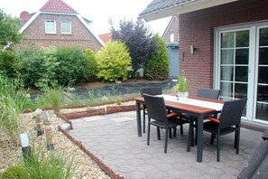 A patio with a table and chairs, surrounded by a garden with various plants and a brick wall. - Frisian happiness in Greetsiel (Greetsiel)