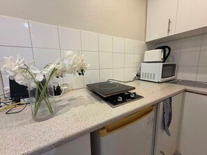 Eine Küche mit weißen Fliesen, einer Mikrowelle, einem Wasserkocher und einer Glasvase mit Blumen auf der Arbeitsplatte.