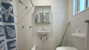 Een badkamer met douche, wastafel, toilet en spiegel boven de wastafel.