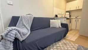 Een moderne woonkamer met een grijze bank, een kamerkleed met patroon en een keuken in de achtergrond.
