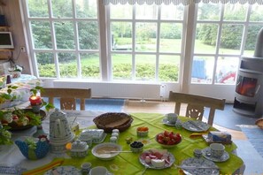 Ein Esstisch, gedeckt mit Tellern, Schüsseln und Tassen, ein Teekessel und ein Obstkorb.