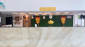 Zona de recepción con mostrador de mármol, cartel de recepción y adornos religiosos.