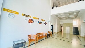En entréhall med en receptionsdisk, träbänkar, ett glasbord, klockor och väggdekorationer med stadsnamn.
