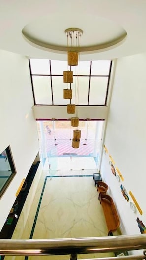 A spacious interior with a high ceiling, a hanging light fixture, a large window, and a marble floor. - Hotel Sona Mina (Tiruchirapalli)
