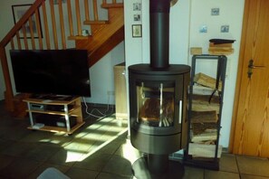 Ein Wohnzimmer mit Fernseher, Kaminofen und einer Treppe.