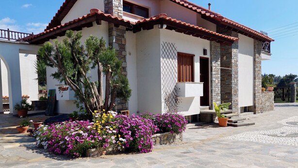 A house with a stone facade, a tiled roof, and a garden with flowering plants. - Primavera Seafront Three Bedroom Apt (Thessaloniki)