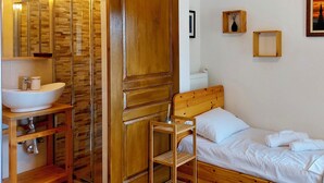 A wooden room with a bed, a wooden chair, a wooden cabinet with a sink, and a wall with framed pictures. - Primavera Seafront Three Bedroom Apt (Thessaloniki)
