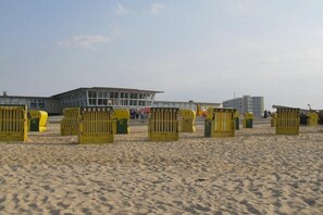A sandy beach with yellow lifeguard chairs and a building in the background. - Holiday Residence Albatros (Cuxhaven-Döse)