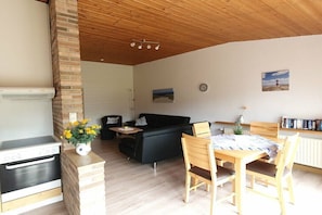 Ein Wohnzimmer mit Sofa, einem Esstisch mit Stühlen, einer Küchenzeile mit Herd und einer Ziegelwand.