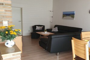 Ein modernes Wohnzimmer mit einem schwarzen Ledersofa, einem Holztisch und einem kleinen Beistelltisch mit einer Vase voller gelber Blumen.