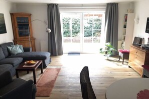 Een woonkamer met een bank, salontafel en een eettafel. Er is een kast, een lamp en een plant.