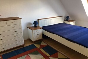 Ein Schlafzimmer mit einem Bett, einem Schminktisch, zwei Nachttischen und einem farbenfrohen Teppich.