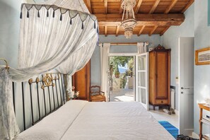Ein Schlafzimmer mit Baldachinbett, Holzbalkendecke, einer Chandelierleuchtre und Blick durch eine offene Tür.