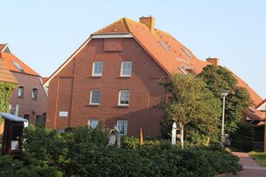 Ein Gebäude aus roten Ziegelsteinen mit einem geneigten Dach, zahlreichen Fenstern und einem Garten mit Büschen und einem Weg.