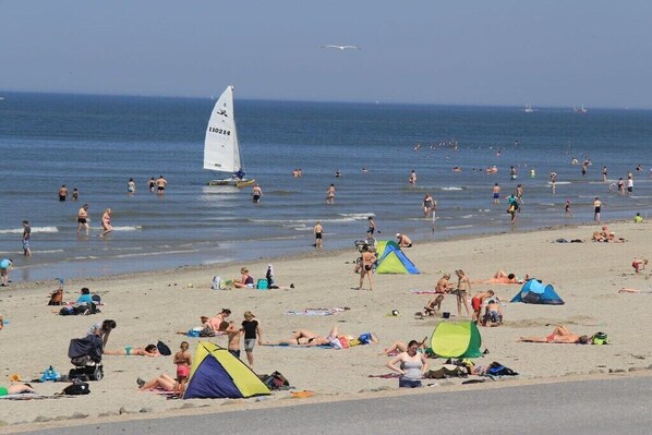 Ein Strand mit badenden Personen, Zelten und einem Segelboot.