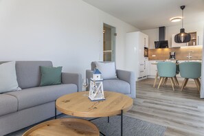 A modern living room with a grey sofa, a round wooden coffee table, and a dining area with two chairs. - A maritime atmosphere, an exclusive setting, and unforgettable views—a vacation (Nordseeheilbad Carolinensiel)