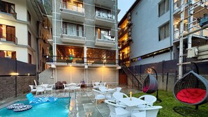 Un área de piscina con mobiliario exterior blanco, una silla colgante y una escalera que lleva a un nivel superior.