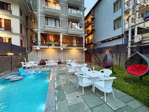 A pool area with white outdoor furniture, a hanging chair, and a staircase leading to an upper level.