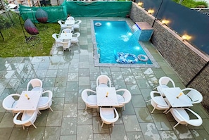 Un área de piscina al aire libre con un deck de cerámica, muebles de mimbre blanco y una pared de piedra.