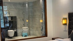 Una habitación de hotel moderna con un espejo grande, ducha, inodoro, cama y mesita de noche.