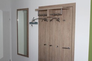 Ein Holzschrank mit Spiegel und einem 'Welcome'-Schild, eine Tür mit Griff sowie ein Kleiderständer mit Haken.