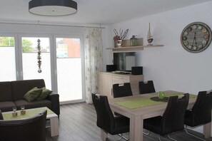 Ein modernes Wohnzimmer mit Sofa, Esstisch, Stühlen, einer kleinen Küchenzeile und einer großen Wanduhr.