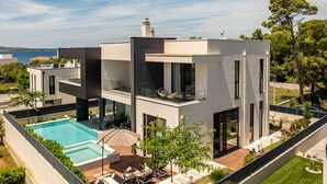 Ein modernes, zweistöckiges Haus mit Swimmingpool, Sitzgelegenheiten im Freien und Meerblick.