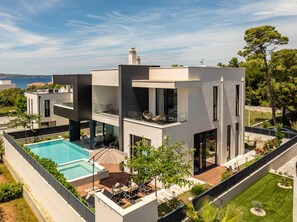 Ein modernes, zweistöckiges Haus mit Swimmingpool, Sitzgelegenheiten im Freien und Meerblick.
