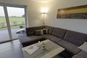 Ein modernes Wohnzimmer mit einem Ecksofa, einem Couchtisch mit einer Zeitung, einer Stehlampe und einem Gemälde an der Wand.