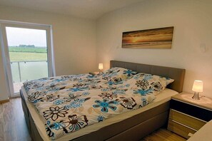 Ein Schlafzimmer mit einem Bett, Nachttischen, einem Gemälde und Blick auf ein grünes Feld durch ein Fenster.