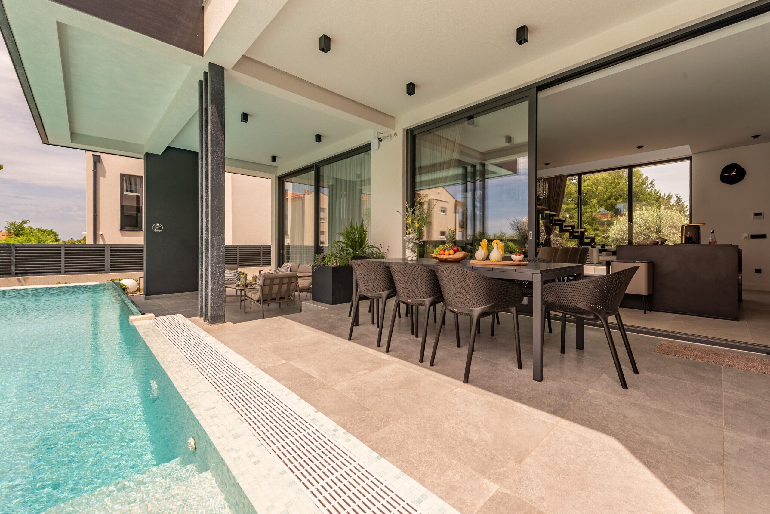 Un espace piscine extérieur moderne, doté d’un coin repas et d’un escalier menant à un niveau supérieur.