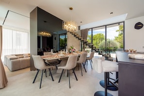 A modern dining area with a chandelier, a staircase, and a view of the outdoors. - Villa Marro ZadarVillas (Privlaka)