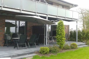 Ein Gebäude mit einer überdachten Terrasse, die Sitzgelegenheiten im Freien und eine hohe, schmale Pflanze bietet.