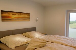 Ein Schlafzimmer mit einem Bett, Kissen, einer Wandleuchte und einem Fenster mit Blick.