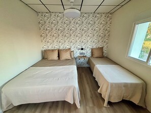 Huoneessa on kaksi erillistä sänkyä, pieni pöytä lampun kanssa, ikkuna ja kuviollinen tapetti.