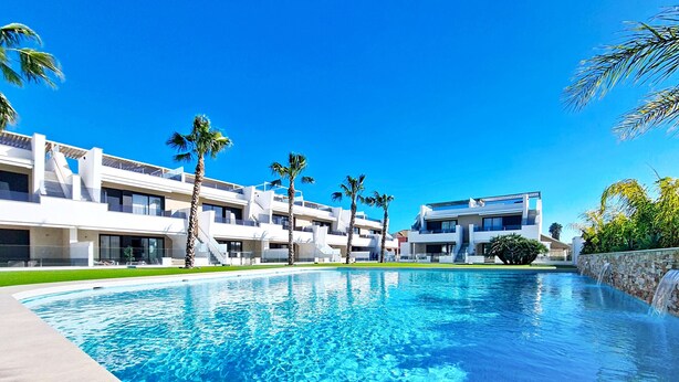 Un hotel moderno con piscina, palme e un cielo azzurro limpido.