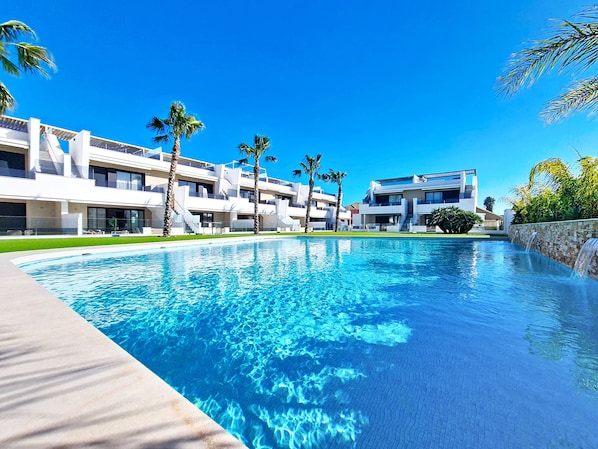 Ein modernes Hotel mit Swimmingpool, Palmen und blauem Himmel.