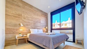 Camera da letto moderna con parete in legno, un letto grande, comodini, una TV e vista sugli edifici attraverso una finestra.