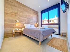 Ein modernes Schlafzimmer mit Holzvertäfelung, einem großen Bett, Nachttischen, einem Fernseher und Blick auf Gebäude durch ein Fenster.