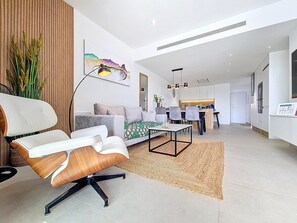 Ein modernes Wohnzimmer mit einer Couch, einem Sessel, einem Essbereich und einer Küche im Hintergrund.