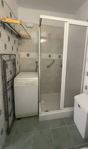 Et lille badeværelse med brusekabine, vaskemaskine og toilet.