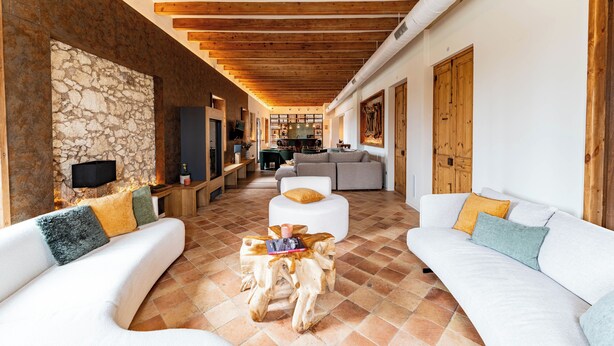 Un salón amplio con una pared de piedra, vigas de madera, un sofá blanco, una mesa de centro de madera y un televisor.