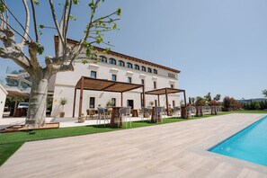 Un edificio con piscina, mobiliario exterior y un árbol.