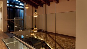 Un interior moderno con una escalera de cristal, una pared de piedra y lámparas colgantes.