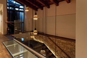 A modern interior with a glass staircase, stone wall, and hanging pendant lights.
