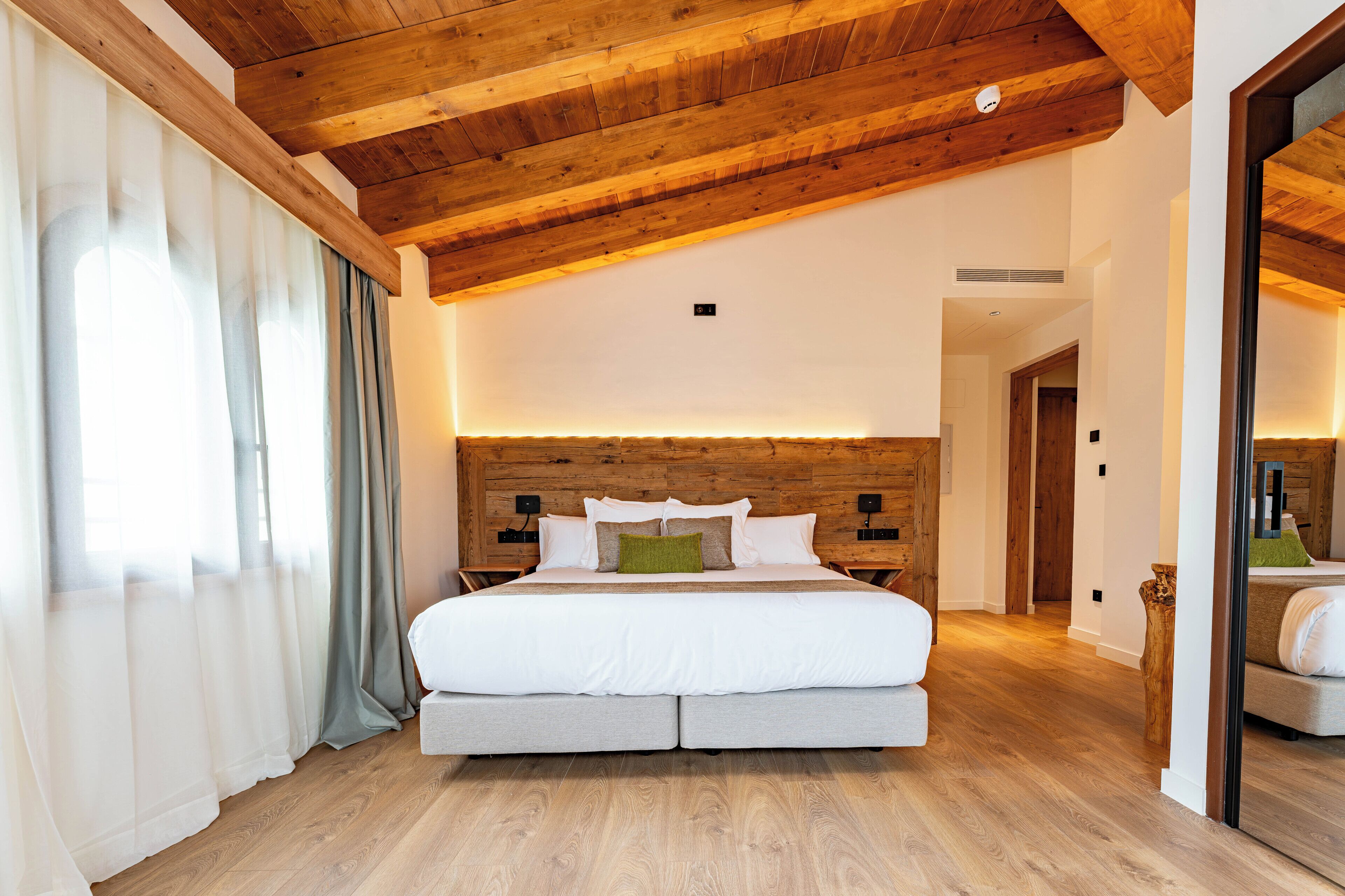 A modern bedroom with a wooden ceiling, a large bed with white bedding, and a wooden headboard.