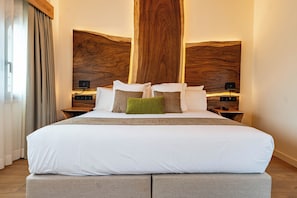 A modern hotel room with a large bed, wooden headboard, bedside tables, and a view of the city.