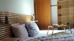Een slaapkamer met een houten hoofdbord, een bed met beddengoed met een patroon, een nachtkastje met een lamp en een garderobe met een schuifdeur.