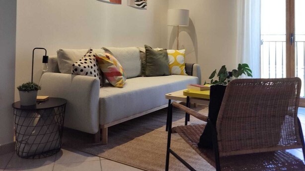 Een woonkamer met een bank, een fauteuil, een lamp en kunst aan de muur.